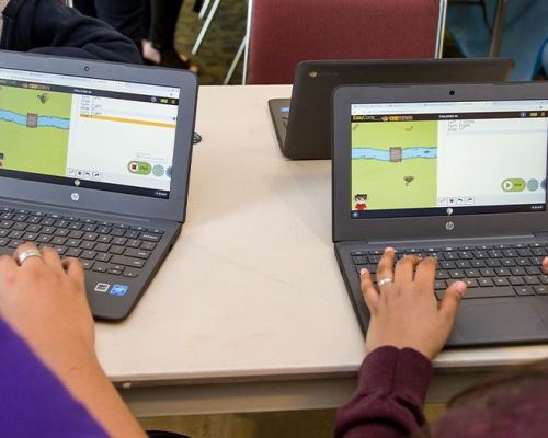 Photo of a group of students at a table using their laptops to learn online.