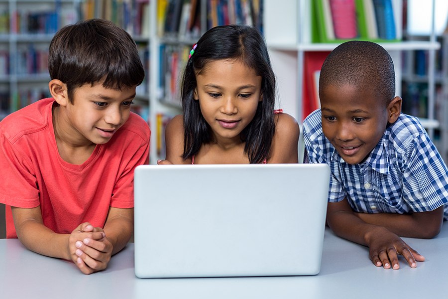 three children on learning.com digital skills program together on laptop in elementary school library 