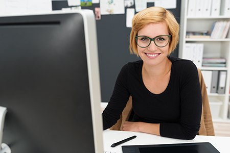 Young woman with glasses sitting at desk in front of computer
