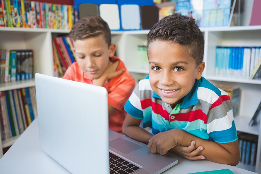 Two elementary aged boys learning digital literacy skills on computer in school library