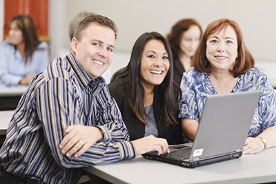Group of learners around computer smiling Group of learners around computer smiling