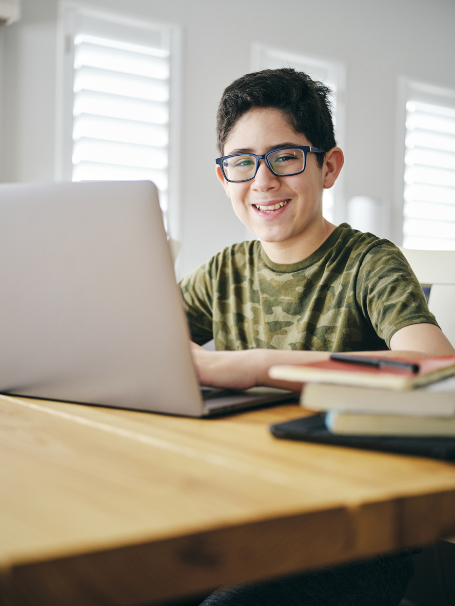 Male student in glasses with computer on desk smiling at camera