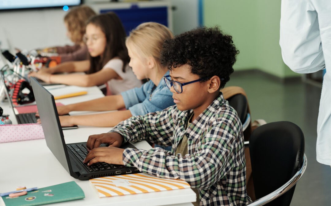 Young elementary students practicing basic computer skills on laptops in computer classroom