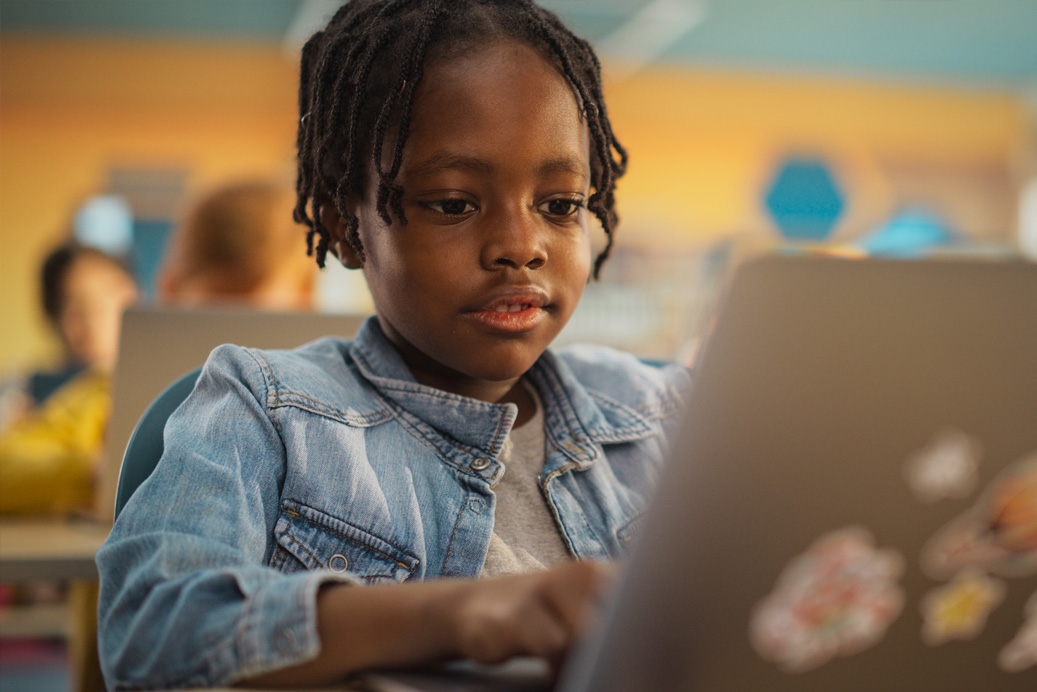 Smiling teacher assisting a student at a computer in a classroom setting
