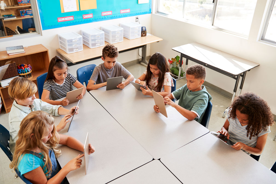 Group of elementary school children using tablets while seated around a table in a classroom