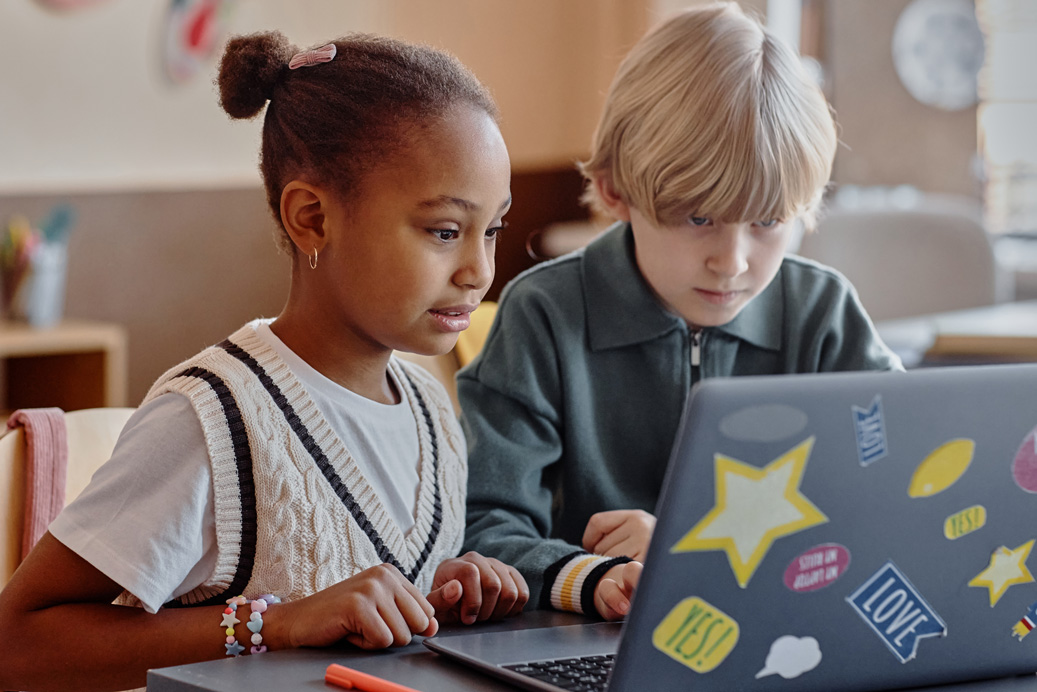 Two young female students thinking like programmers on a laptop in a classroom
